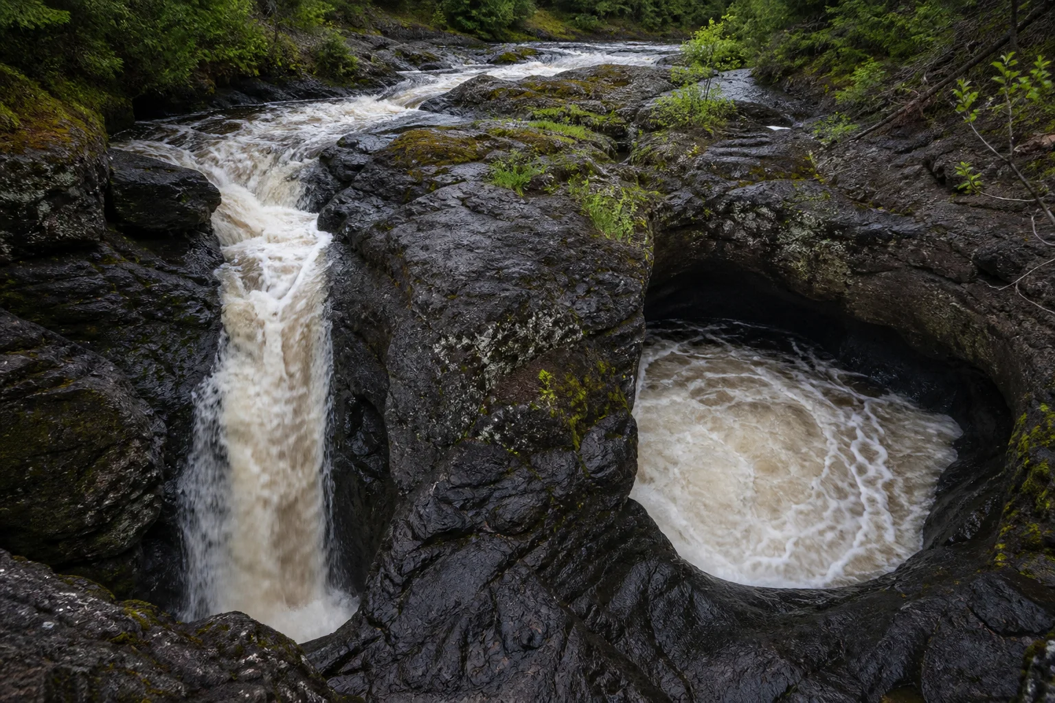 The Brule River divides around a dark volcanic rock knob, with one branch falling and the other churning into a pothole